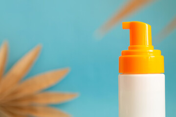 White and yellow sunscreen bottle with cream or lotion on the aqua blue background with palm branches. Spf sun protection, summer skin moisturizer closeup