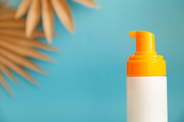 White and yellow sunscreen bottle with cream or lotion on the aqua blue background with palm branches. Spf sun protection, summer skin cosmetic
