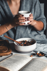 A young woman drinks morning coffee, eats a healthy breakfast and reads a book. Morning routine. Stylish manicure. Correct habits. Holding a cup in his hands - 427206867