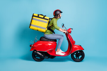 Full length side profile photo portrait of woman delivering big yellow package on red scooter isolated on pastel blue colored background © deagreez