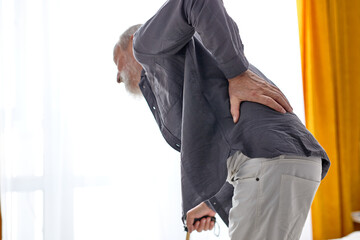 Retired man suffering from back pain at home, having difficulty in getting up from bed
