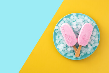 Strawberry popsicles and crushed ice on blue plate and yellow and blue background