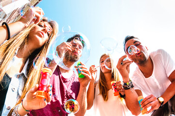 Young friends having fun playing with soap bubbles at spring break time - Friendship concept and...