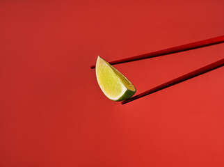 Red Chinese chopsticks derazh a lime wedge. Red on red. Cooking ingredients for Asian food. Spicy food. Red background. Asian products. Ingredient for pho bo soup. Macro photography of food.