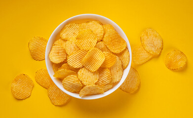 Ridged potato chips in bowl on yellow background