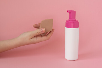 Facial cleansing sponges in a woman's hand with white bottle, face soap, foam, on pink background