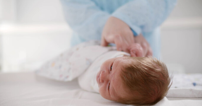 Close Up Of Happy Young Mother Swaddling Baby On Table