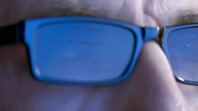 The programmer's (hacker's) glasses reflect the computer program code on which he is working (or trying to hack). Macro. Close Up