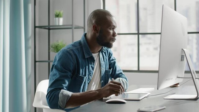 Bald Afro-american engineer draws scheme on tablet at desk