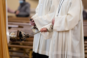 A minister in a white robe holds a censer during Holy Mass in the Catholic Church