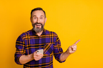 Portrait of handsome trendy amazed cheerful guy using gadget demonstrating copy space isolated over bright yellow color background