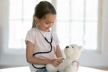 Small Caucasian girl child hold stethoscope listen to fluffy toy heart breath act as doctor. Cute...
