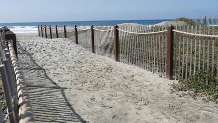 Pacific ocean coast, greenery and wooden picket fence on sea shore. Blue water waves on sunny...