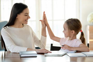 Smiling young Caucasian mother and little 7s daughter give high five for finished homework...