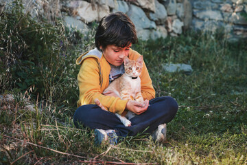 Naklejka na ściany i meble kid sitting on the grass with his kitten
