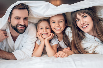 Smiling family in white robes lying in bed and having fun