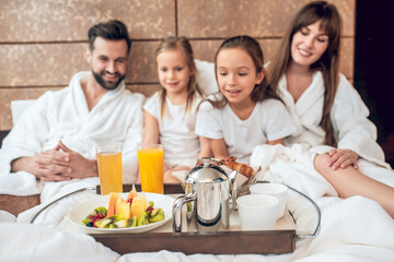 Family in white robes lying in bed and having breakfast