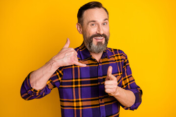 Photo of happy positive mature man make call me gesture point finger you smile isolated on yellow...