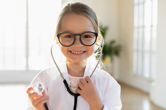 Close up headshot portrait of cute little Caucasian girl child in medical uniform stethoscope play act doctor. Profile picture of small smiling kid have fun enjoy hospital game. Healthcare concept.