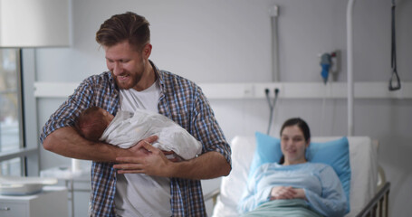 Nurse giving newborn son wrapped in blanket to young father in hospital