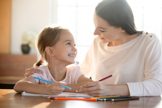 Smiling little girl child have fun drawing painting with caring young Caucasian mother at home. Happy mom and cute small daughter enjoy creative art activity together. Hobby, creativity concept.