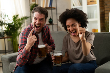 Boyfriend and girlfriend drinking beer at home. Happy couple watching sports game on tv...