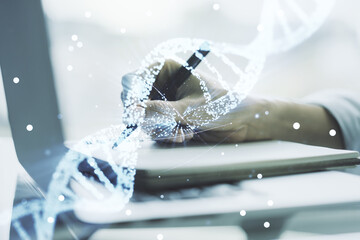 Creative DNA sketch and hand writing in notepad on background with laptop, biotechnology and...