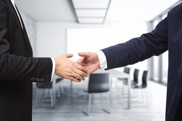 Two businessmen shake hands on the background of bright conference room, investing concept, close up