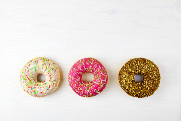 Three colorful donuts on a white wooden background.