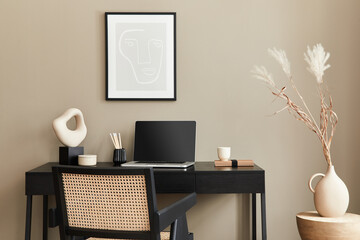 Stylish composition of home office interior with black wooden desk, chair, dried flower in vase, laptop, mock up poster frame, cup of coffee, clock and elegant office accessories. Template.