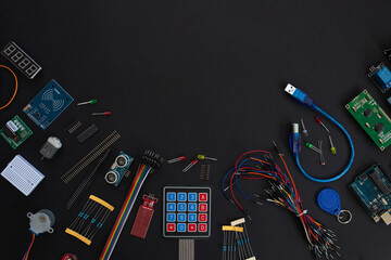 various microcircuits, controllers, sensors, parts, motherboard, cable, wires and a soldering iron on a muted black background.. copy space. flatlay