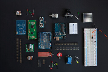 various microcircuits, controllers, sensors, parts, motherboard, cable, wires and a soldering iron on a muted black background.. copy space. flatlay
