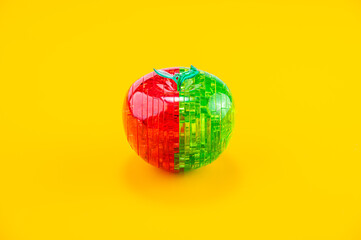 Assembled red-green plastic puzzle in the shape of an apple, on the yellow background.