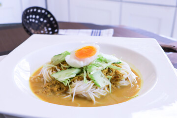 image of Kanom Jeen Thai herbs rice noodles with yellow curry fish sauce served with boiled egg and cucumber with slice of green cabbage.