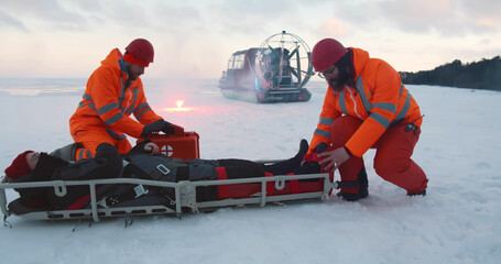 Lifeguards carrying victim on stretcher and loading in hovercraft on frozen lake