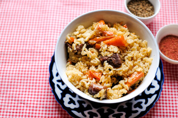 Bowl of asian food pilaf with rise, carrot and spices at table  background