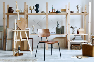Unique artist workspace interior with stylish teak commode, wooden easel, bookcase, artworks, painting accessories, decoration and elegant personal stuff. Modern work room for artist. Template.