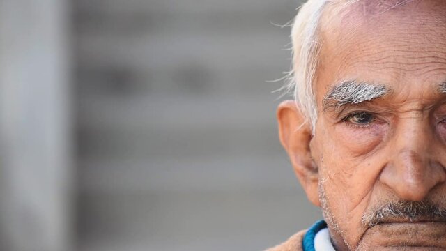 Portrait of elderly man's half face over grey background at home with copy space. Old Indian man portrait. Serious grey haired man seriously looking at camera