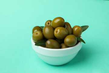 Bowl of green olives and leaves on mint background