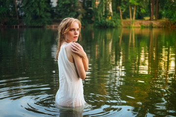A beautiful girl in a wet dress bathing in the lake.