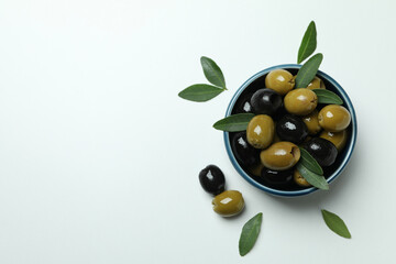 Bowl of olives and leaves on white background, top view