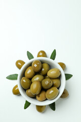 Bowl of green olives and leaves on white background