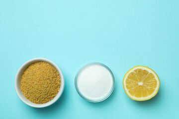 Bowls with mustard powder and acid powder, and half of lemon on blue background