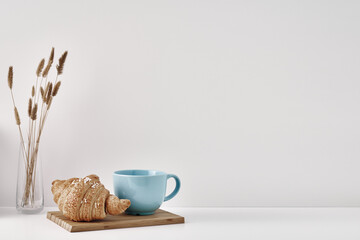 Croissant and a mug on a wooden stand, a vase and a pot with a plant on the books, white background. Eco-friendly materials in interior decor, minimalism. Copy space, mock up.