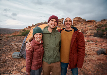 Group of young happy friends standing outside tent posing during camping in winter clothing
