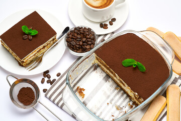Traditional Italian Tiramisu dessert in glass baking dish, portion on plate and cup of coffee isolated on white background