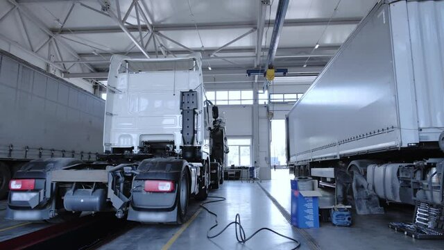 Panorama at the service station of trucks with semi-trailers and refrigerators. Lorry are in the truck service on the inspection pit.