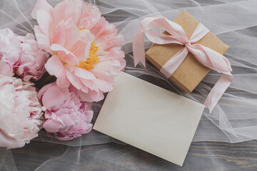 Beautiful peony bouquet, gift and card on soft tulle  on dark wood, top view. Happy Mothers day