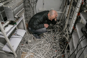 The man is in a plundered server room. A sad technician sits near a pile of wires and holds his...