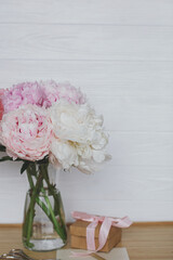 Beautiful peony bouquet in vase, gift box, greeting card on wooden background, copy space